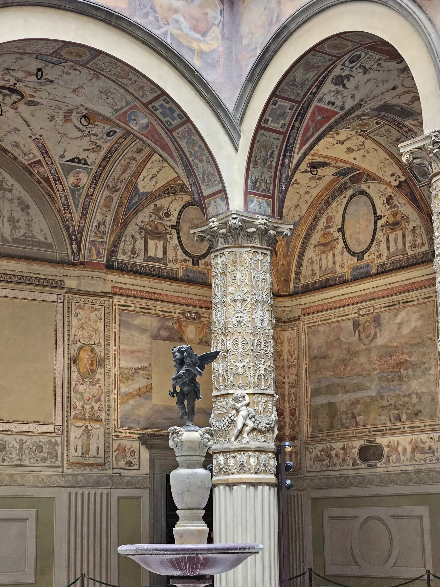 Frescoed vaulted loggia with a carved column and marble statue
