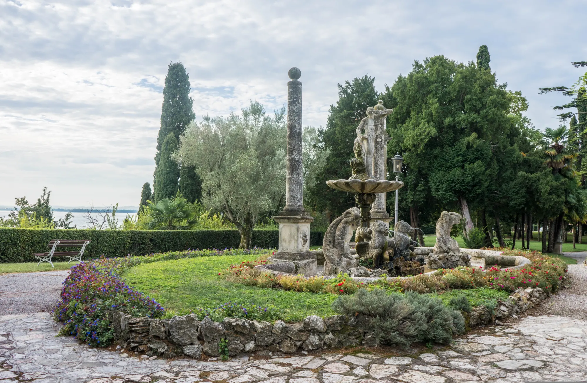 Villa garden with a stone fountain and cypresses, the lake beyond