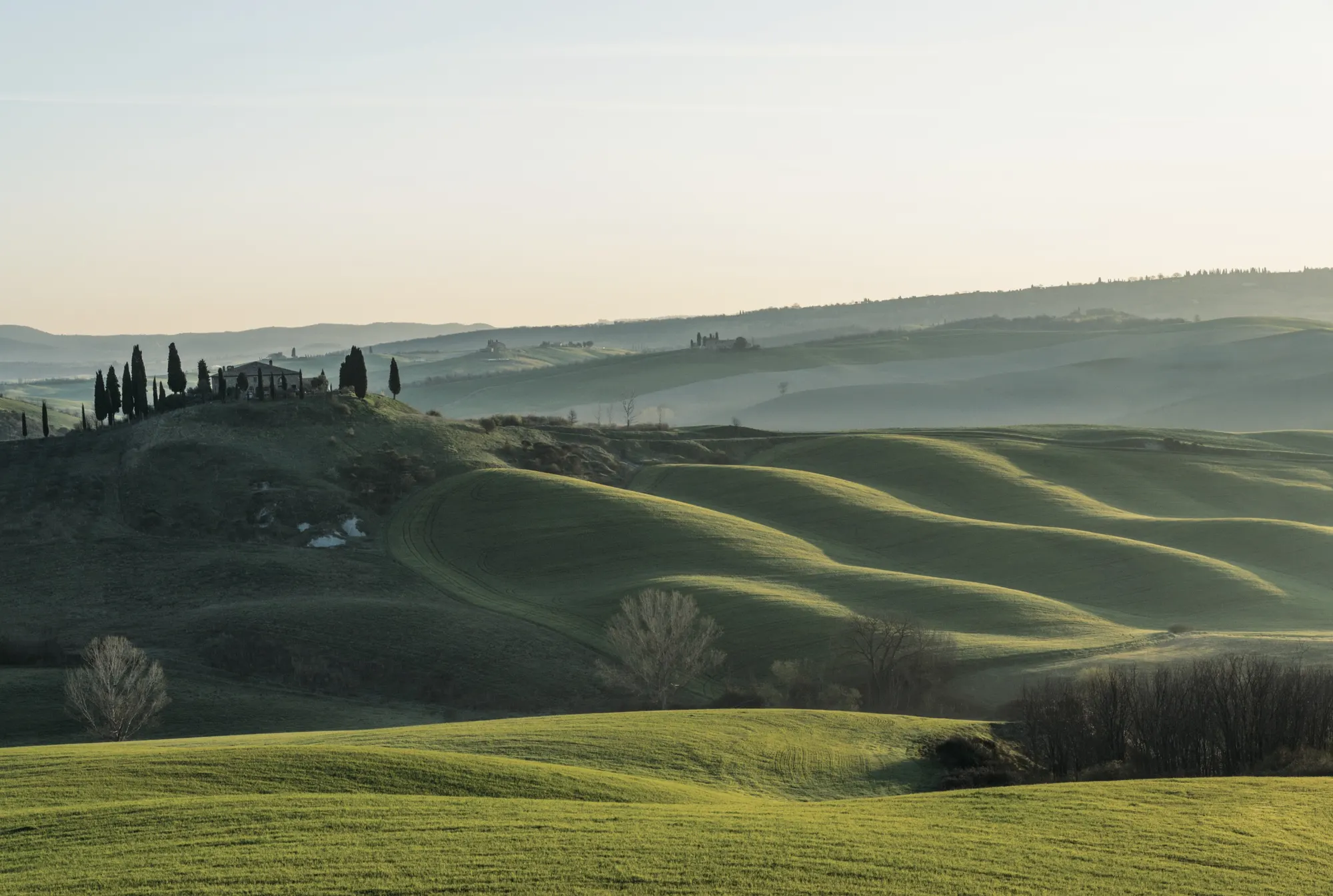 Rolling Tuscan hills at dawn, a farmhouse and cypresses on the ridge