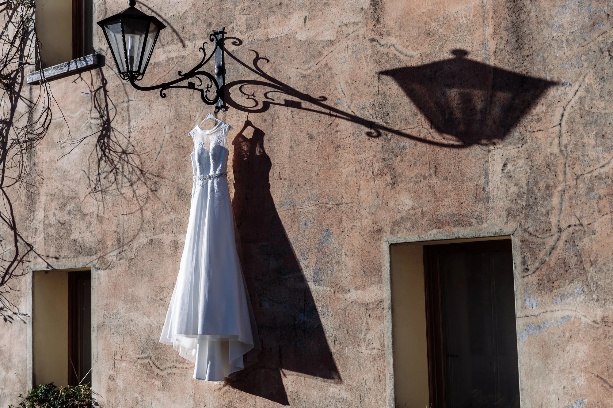 Wedding dress hanging from a wrought-iron lantern on a stone wall